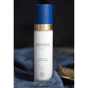 Pureday En hvid hudpleje Økologisk ansigts serumflaske mærket "esenka infinity collection" med en marineblå hætte, placeret på en tekstureret grå stofbaggrund, let sløret træobjekt i forgrunden. Pureday En hvid hudpleje Økologisk ansigts serumflaske mærket "esenka infinity collection" med en marineblå hætte, placeret på en tekstureret grå stofbaggrund, let sløret træobjekt i forgrunden.