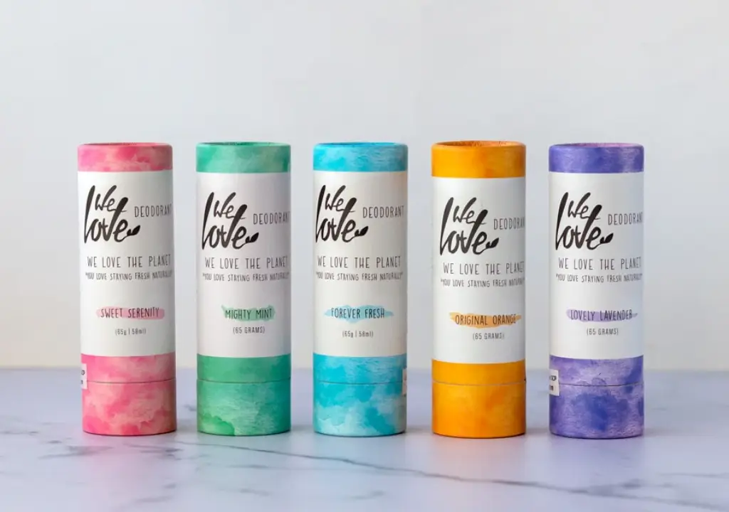 Pureday Fem cylindriske deodorantpinde er arrangeret på række på en marmoroverflade. Hver har en pastelfarvet etiket med forskellige dufte: Sweet Serenity, Mighty Mint, Forever Fresh, Original Orange og Lovely Lavender. Omfavn naturlig velvære med "We Love The Planet" fremtrædende vist.